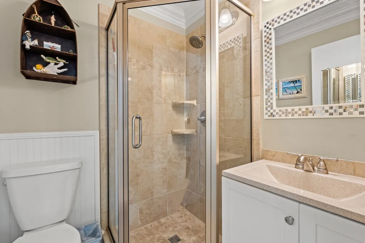 A modern bathroom scene with a glass-enclosed shower, vanity with sink, and a decorative shelf. The surfaces are clean and the lighting is soft, creating a fresh and inviting environment for personal routines.
