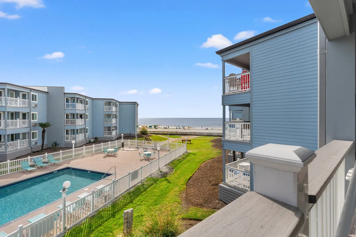 The hero image showcases a sparkling swimming pool surrounded by a lush lawn, with a stunning view of the sandy beach and ocean just steps away. A private balcony overlooks both the pool and the coastline, inviting guests to relax while soaking in panoramic seaside vistas. The scene is bathed in warm, inviting light, promising unforgettable sunsets and tranquil mornings.
