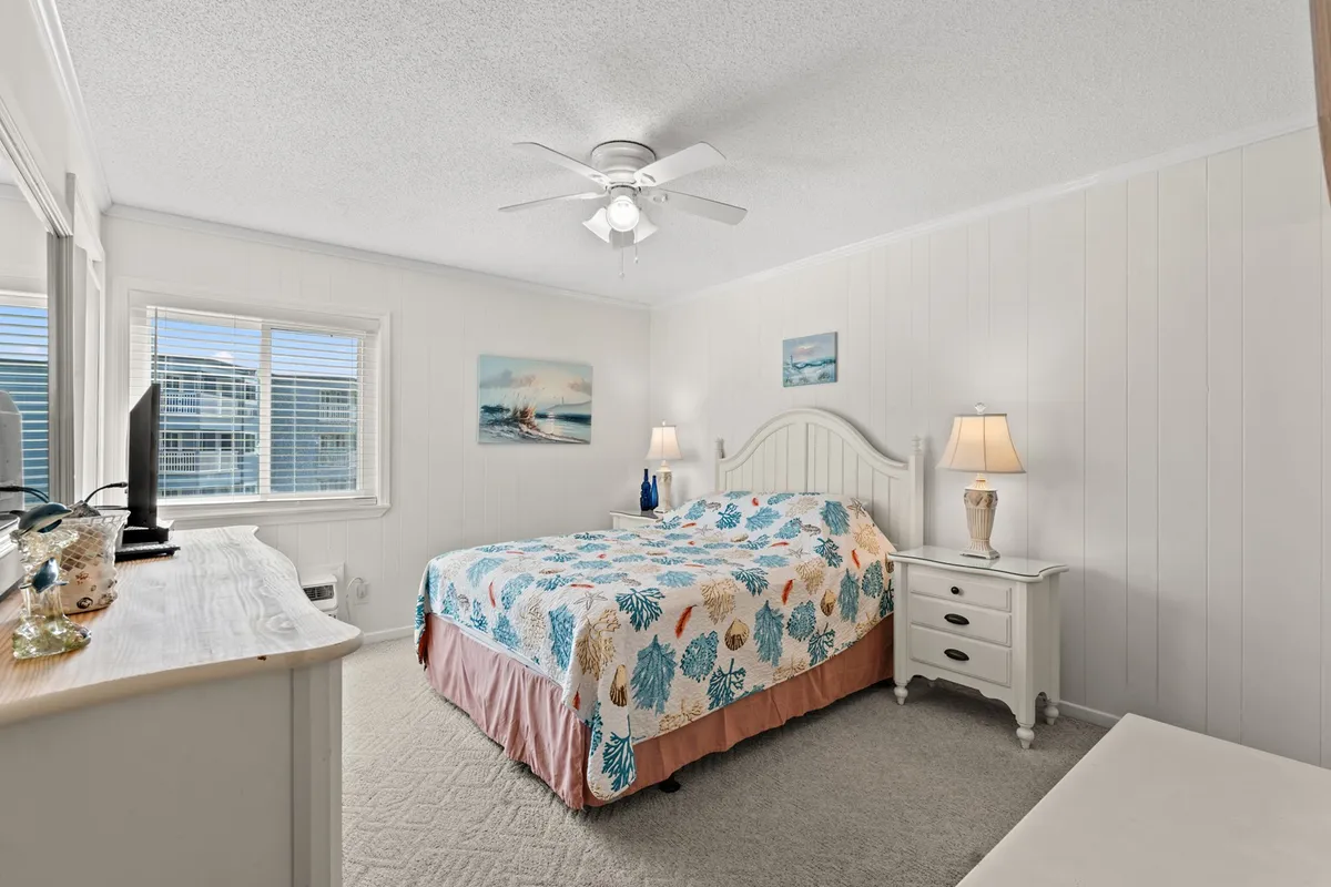 This image features a bed dressed in a colorful quilt, flanked by nightstands with lamps and adorned with wall art above the headboard. The scene is softly lit, creating a serene atmosphere ideal for restful sleep.
