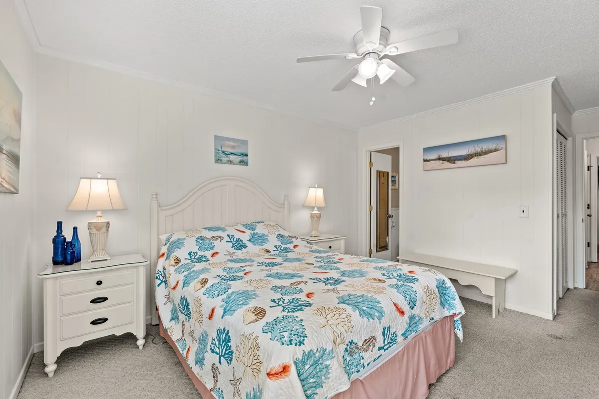 A warmly lit bedroom with a bed featuring coral-patterned bedding, matching nightstands with lamps, and playful artwork on the walls. The room feels cozy, perfect for unwinding after a day at the beach.