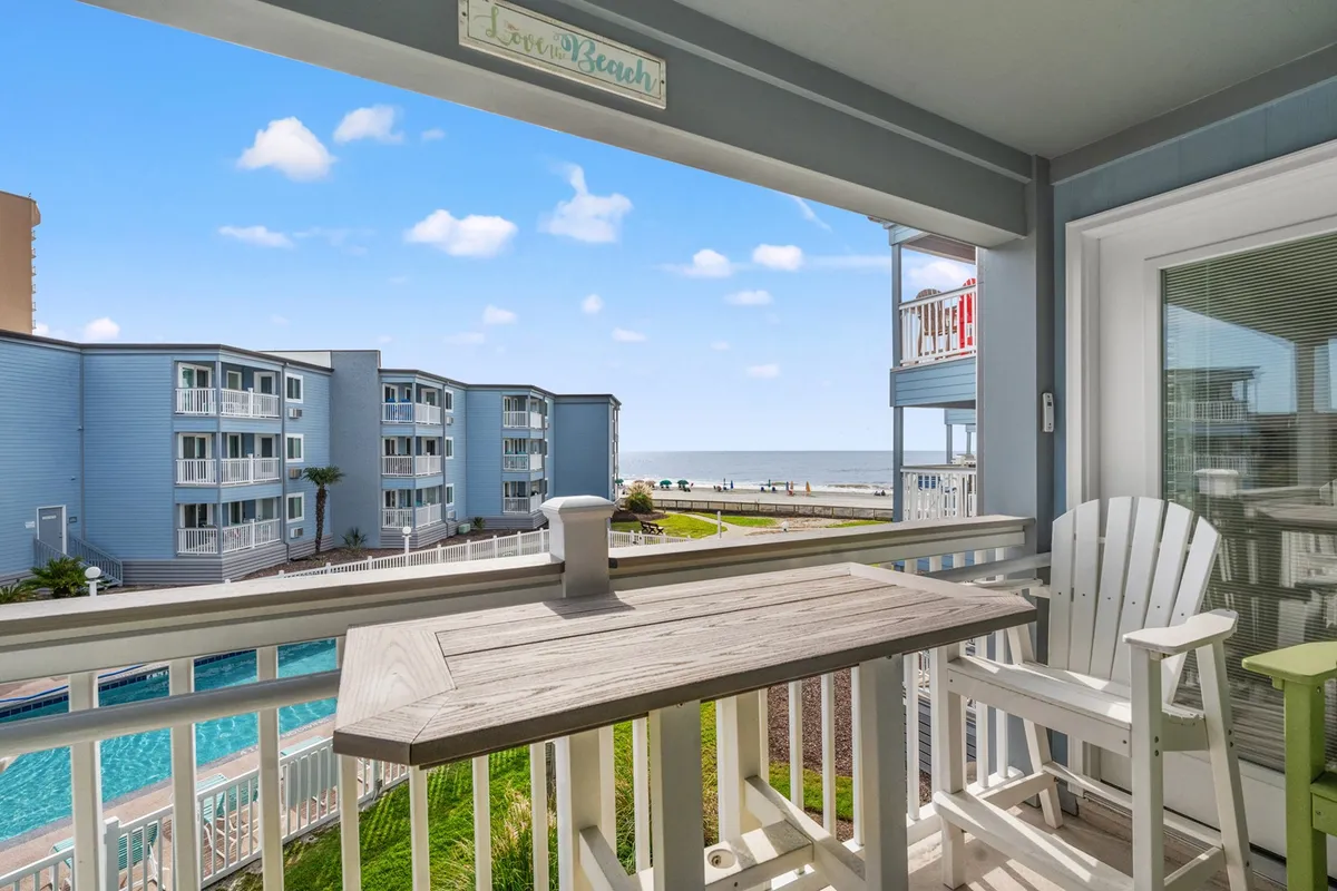 This image features a serene ocean view from a private balcony, complete with comfortable seating and a glimpse of the swimming pool below. The inviting scene captures the essence of relaxing mornings with coffee, group conversations, or unwinding after a day of activities.