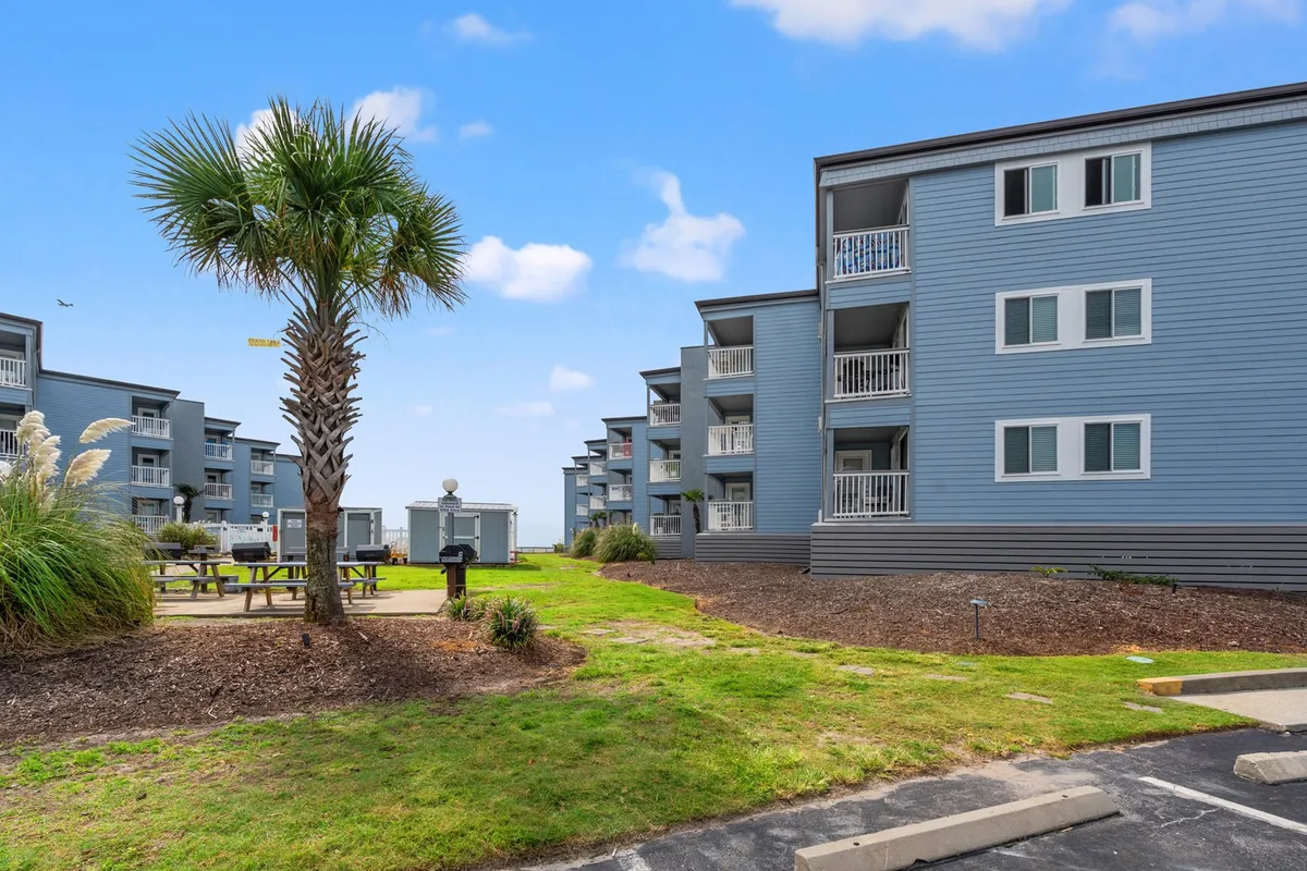 An exterior shot showing palm trees, a relaxed outdoor seating area, and the building facades, all set under sunny skies. The arrangement is ideal for social gatherings, whether casual chats or evening get-togethers, and conveys a welcoming, sunny atmosphere.
