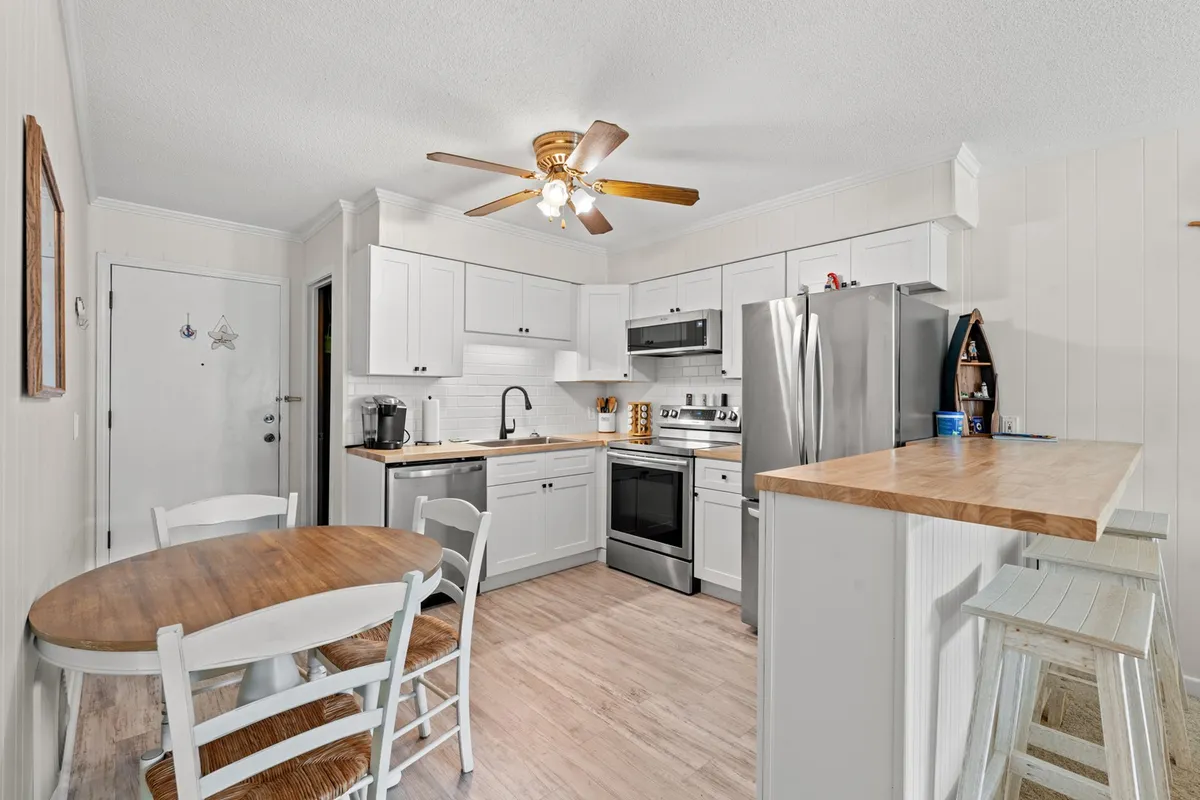 A bright, welcoming kitchen with a central island, round dining table, white cabinetry, and stainless steel appliances. The space is arranged for easy movement and conversation, ideal for cooking together and sharing casual meals.