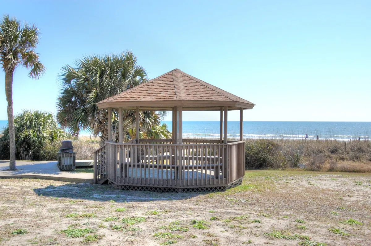 A scenic exterior view featuring a charming gazebo overlooking the ocean, surrounded by palm trees. The space invites guests to relax, enjoy picnics, and savor the coastal views, highlighting the natural beauty accessible from the property.