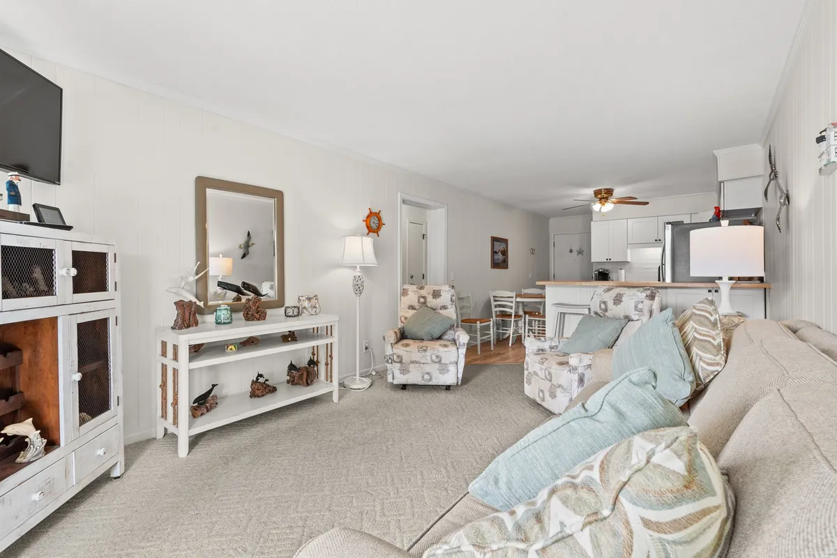 A spacious, open-plan living area featuring a comfortable sofa, decorative chairs, a coffee table, and a television, with the dining area visible in the background. Warm lamps and natural light fill the space, creating an inviting atmosphere perfect for socializing, relaxing, or sharing meals.