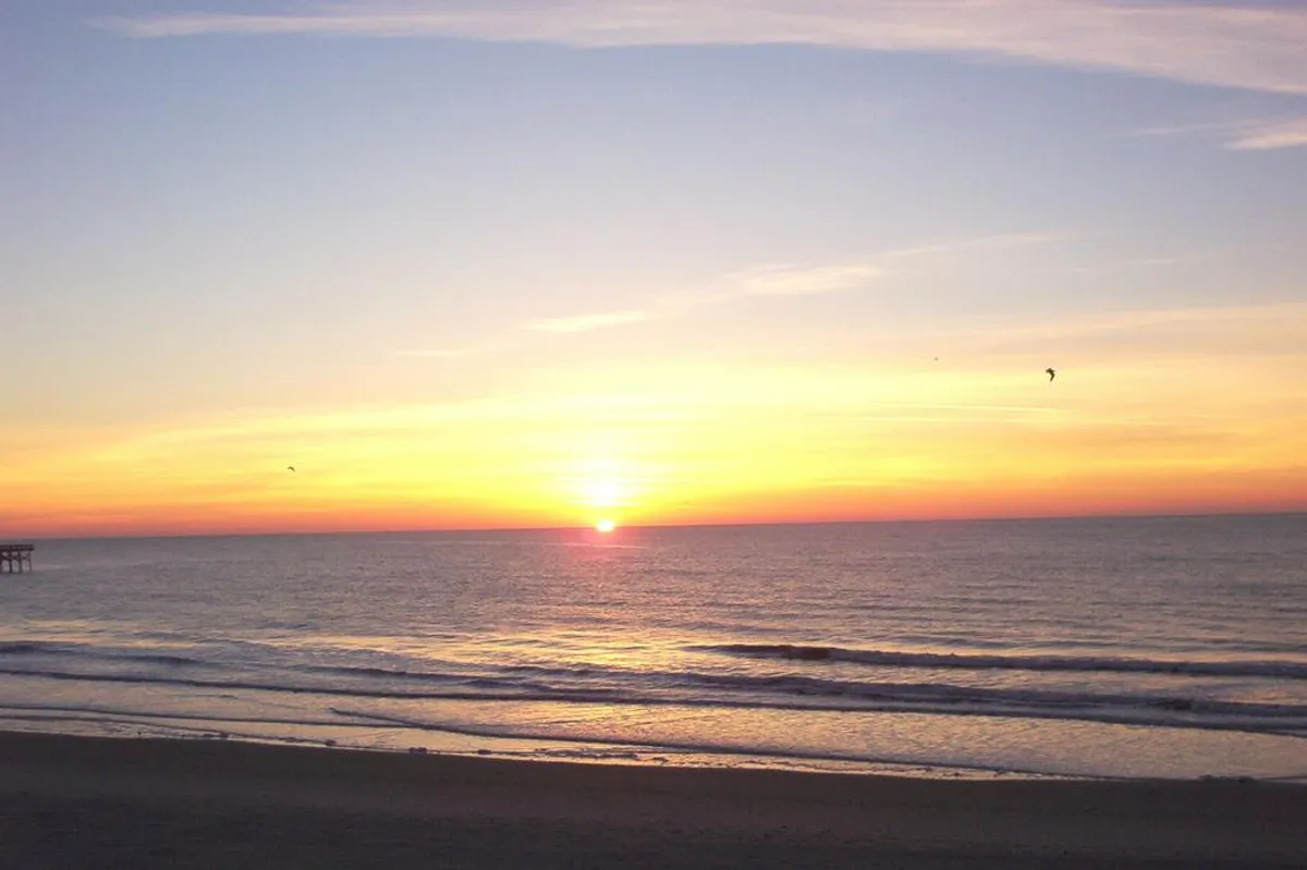 A breathtaking coastal sunset scene with gentle waves and a distant pier, evoking a sense of tranquility and connection. The soft colors and serene mood invite reflection and relaxation after a night out.