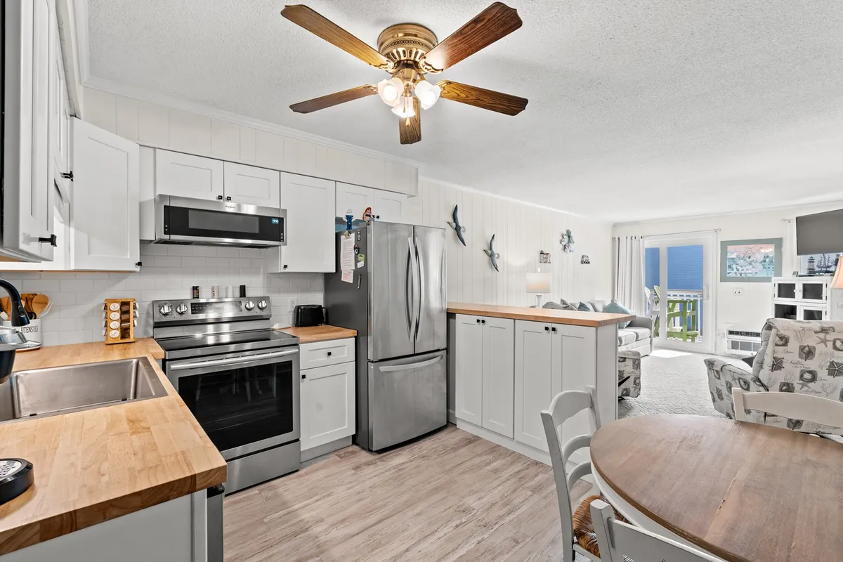 A modern kitchen with a prominent island topped with a butcher block, gleaming stainless steel appliances, a charming dining area, and playful decorative touches. Large windows invite natural light, making the space ideal for family meals and memorable gatherings.